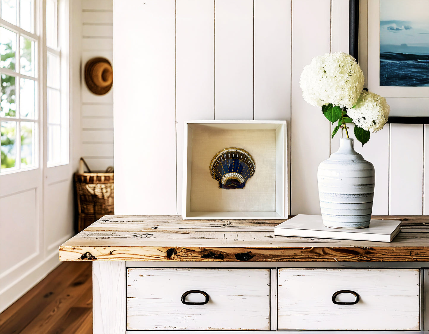 Wooden console table with a vase of flowers and framed picture against a white paneled wall.