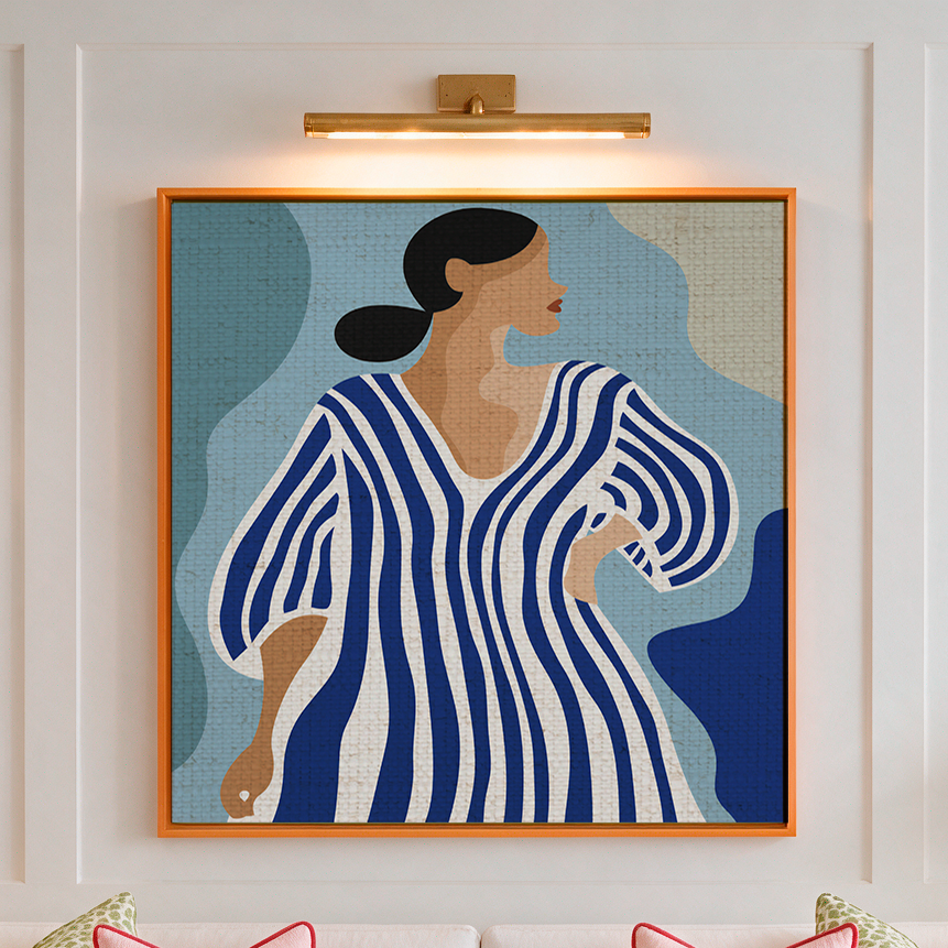 A framed art print featuring a stylized woman in a blue and white striped dress, displayed on a white paneled wall above a white sofa in a beautifully decorated living room.