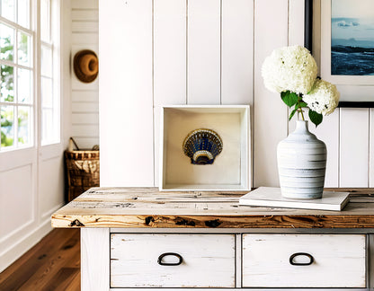 Wooden console table with a vase of flowers and framed picture against a white paneled wall.