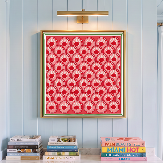 A framed square art print featuring a red and pink pattern of concentric circles and crescents, hung on a light blue paneled wall above a marble countertop with books.