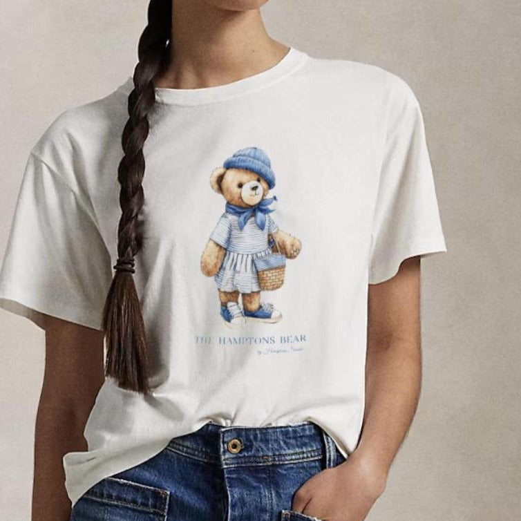 Person wearing a white t-shirt with a teddy bear graphic and blue jeans against a beige background